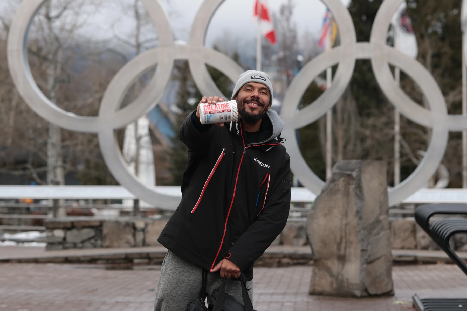 Davidson smiling and holding a creatine container in front of the Olympic rings