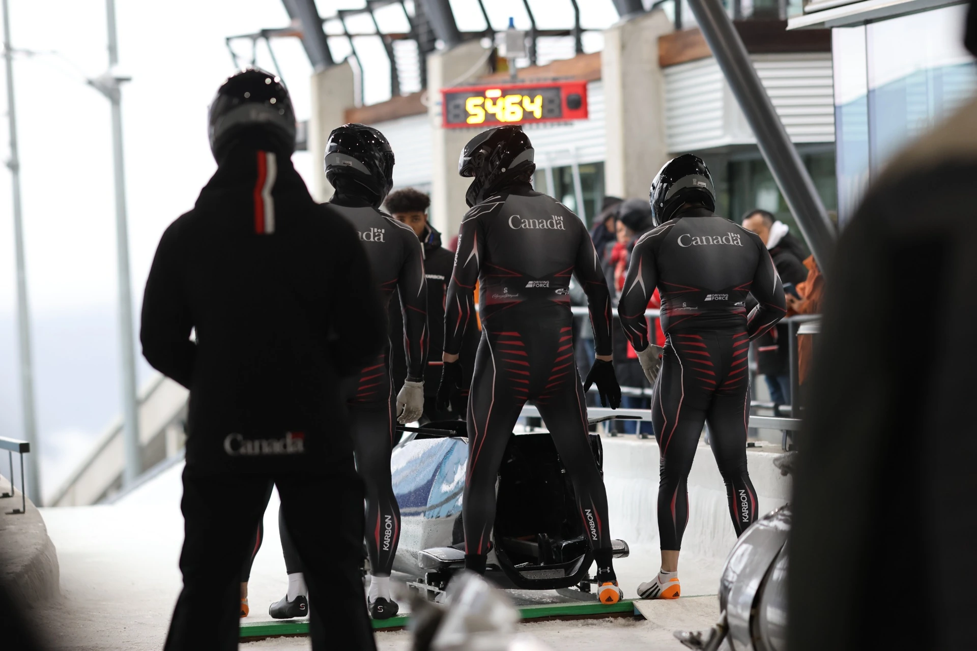 Team Canada athletes preparing beside their bobsled at the start